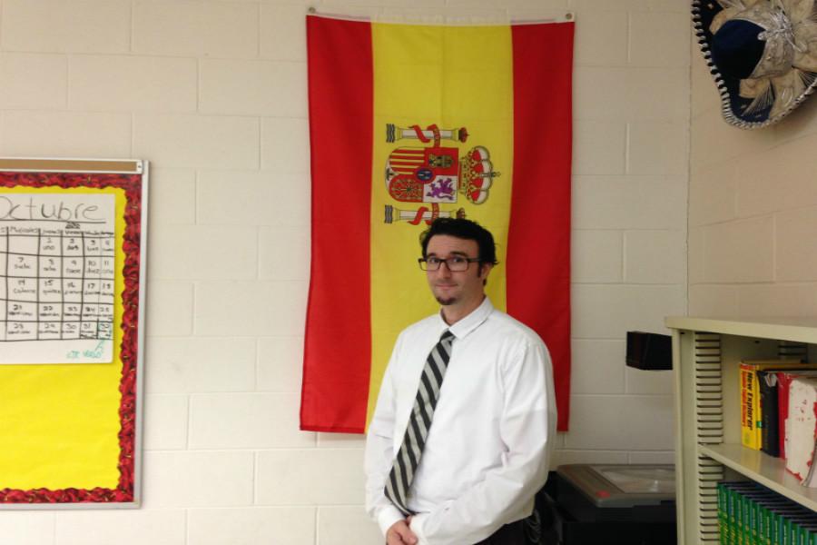 St. Denis stands in front of the Spanish flag in his classroom.