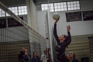 Middle Hitter Elise Sepe jumps to hit the ball right while her teammates and opponents watch in suspense.