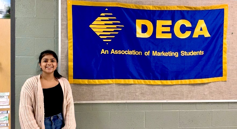 DECA president Shelly Singhal standing next to the DECA board. 