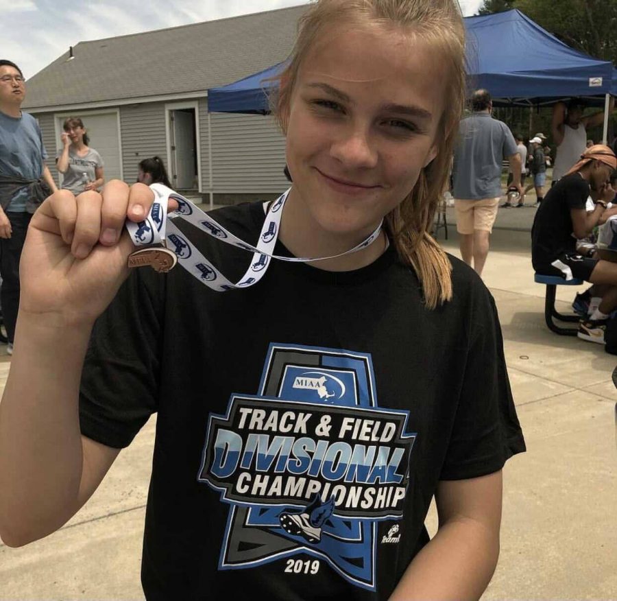 Wahlquist holding up 3rd place medal for long and high jump in the 2019 track and field divisional championships.