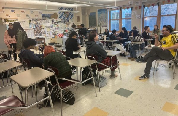 German teacher Herr Welch sits down to have a whole class discussion in a packed classroom. 