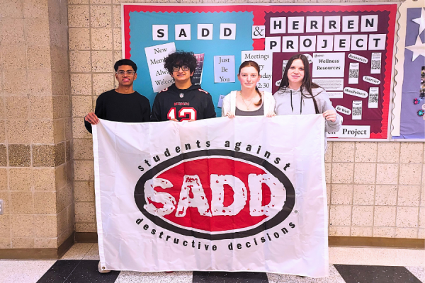 SADD members (left to right) Vineeth Badvelu, Irith Midha, Avery Ganz, and Makayla Cassie hold up their banner in front of their club bulletin board, which advertises their upcoming semi-formal.