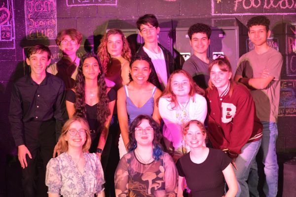 The cast and crew of Voices From The High School huddle together for a group photo in the black box theater. 