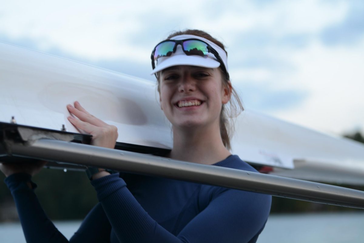 Aeder poses for a photo as she carries her boat back after finishing practice.