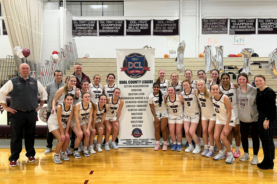 Girls' basketball team and their coaches pose for a photo in front of the DCL banner after becoming undefeated DCL champions