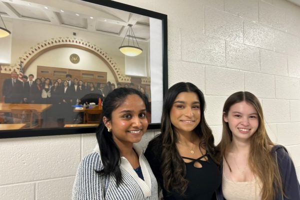 WA Mock Trial captains Finney, Mehta, and Phan (from left to right) smile in front of a framed photo of their 2023 Elite 8 Tournament.