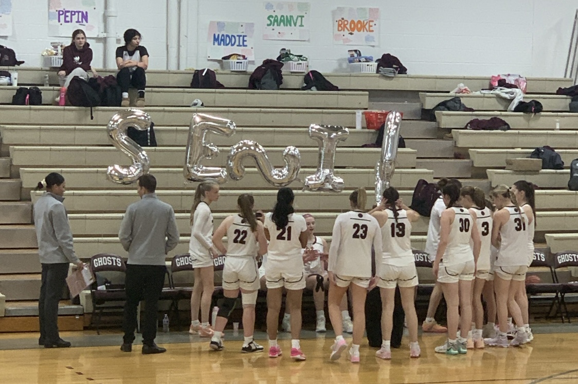 The girls' basketball team gathers in a huddle, surrounded by senior night decorations.