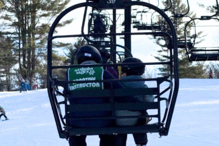 An adaptive ski instructor accompanies a student up the chairlift.